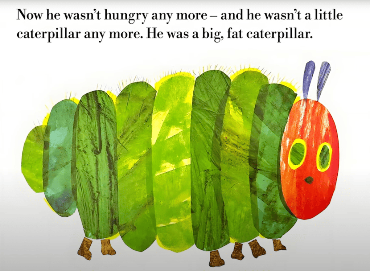 A large, colorful caterpillar  from <em>The Very Hungry Caterpillar</em> (1969) with a red head, yellow-rimmed green eyes, purple antennae, and a segmented green body stands on stubby brown legs. Above the caterpillar, the text reads: "Now he wasn’t hungry any more – and he wasn’t a little caterpillar any more. He was a big, fat caterpillar."