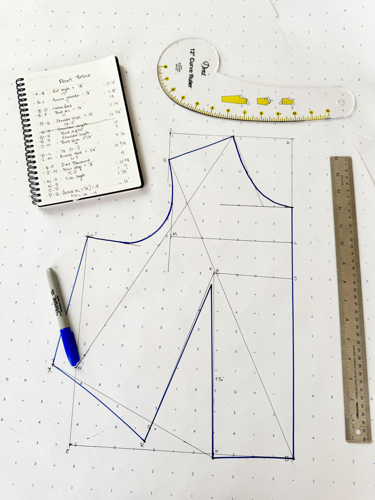 a sketch of a bodice block on grid paper with a ruler and notebook